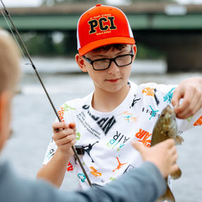Young man holding a fish he just caught in one hand and a pole in the other hand