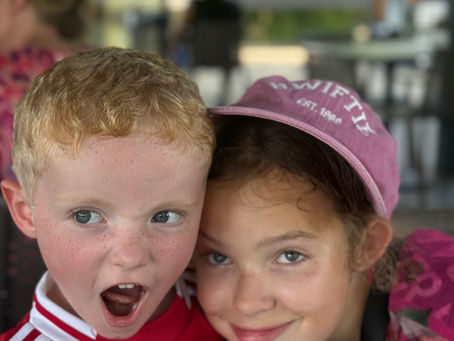Two children, a boy and a girl, pulling funny faces for the camera. They are making silly expressions before smiling, showing playful summer chaos at home.