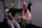 Pole instructor teaching a students how to invert, the teacher is spotting the student and the pole is pink