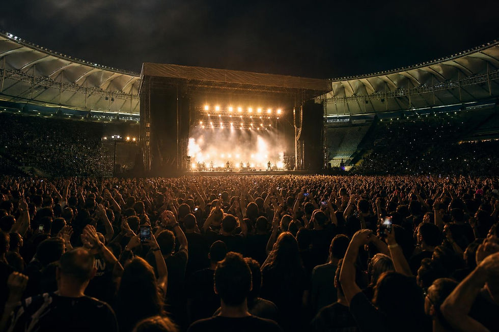 Palco de estádio lotado à noite com luzes e público, representando show de rock em grande arena.