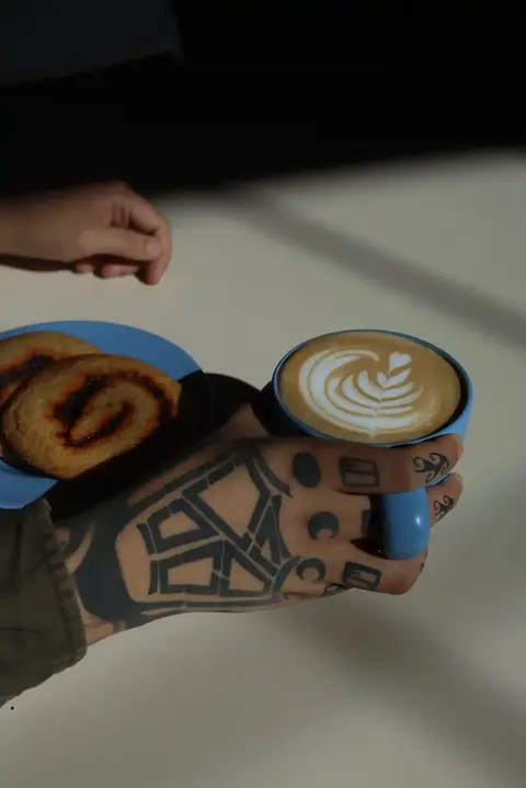 hand with henna art holding a coffee drink next to a plate of desserts