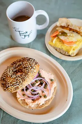 cup of coffee with a breakfast sandwich and a bagel with cream cheese, salmon, onions and capers