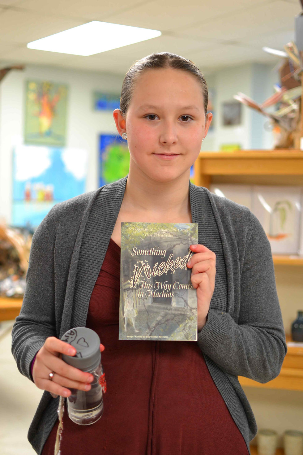 Aiyanna R. Muise smiles while holding a copy of the 2026 Machias Arts Council Flash Fiction anthology at the book launch celebration.