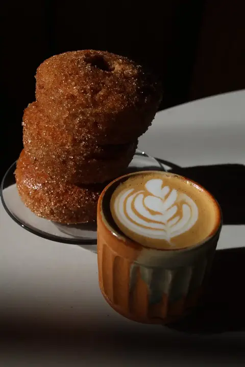 coffee drink in a mug next to a plate with baked doughnuts