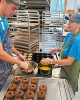 man and woman preparing a tray of baked doughnuts