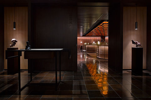 Welcome area of a dark restaurant with round stools and orange squares ceiling