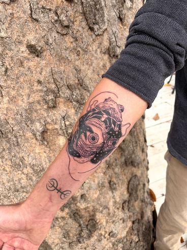 A custom black and grey surreal skull illustration featuring flowing organic forms, exposed anatomy, and abstract elements that blur the line between life and decay. Fine linework, smooth shading, and bold black accents create depth and texture, giving the piece a striking, illustrative feel while allowing the composition to flow naturally along the forearm.