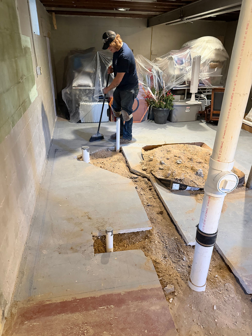 Underground plumbing rough-in in a Delafield, WI basement. New PVC pipes are set in the trench through the cut slab, belongings are covered, and the floor is swept clean before we leave.