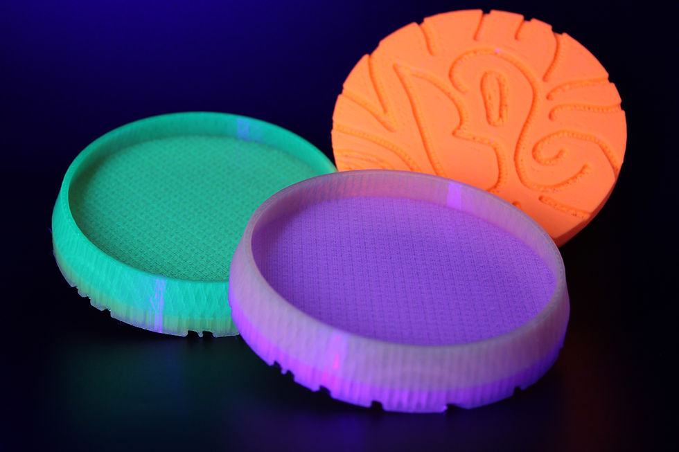 three colorful circular 3D-printed trays glowing under UV light on a dark background, wide landscape