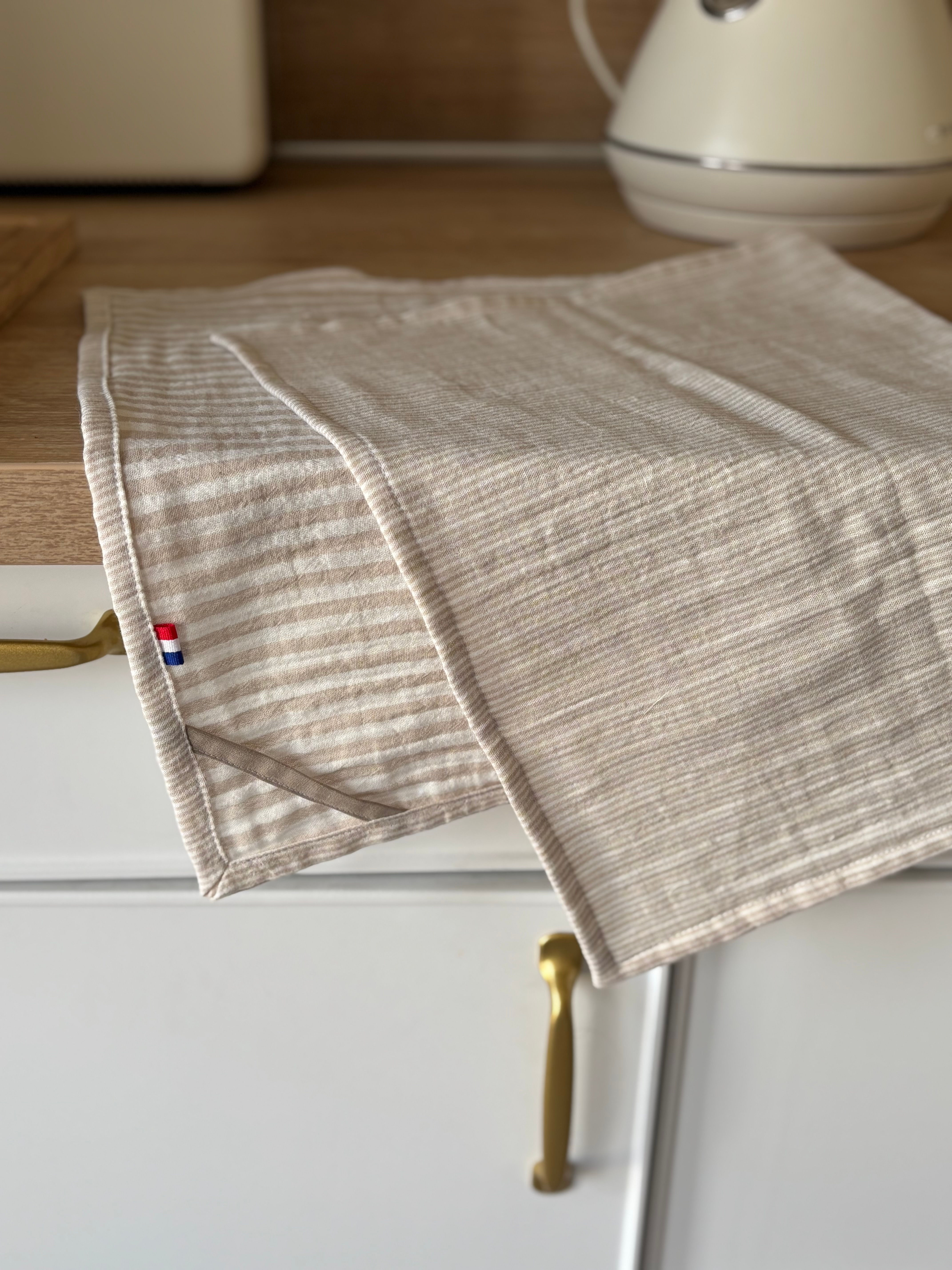 Un torchon beige et blanc à rayures, avec un drapeau français au coin.