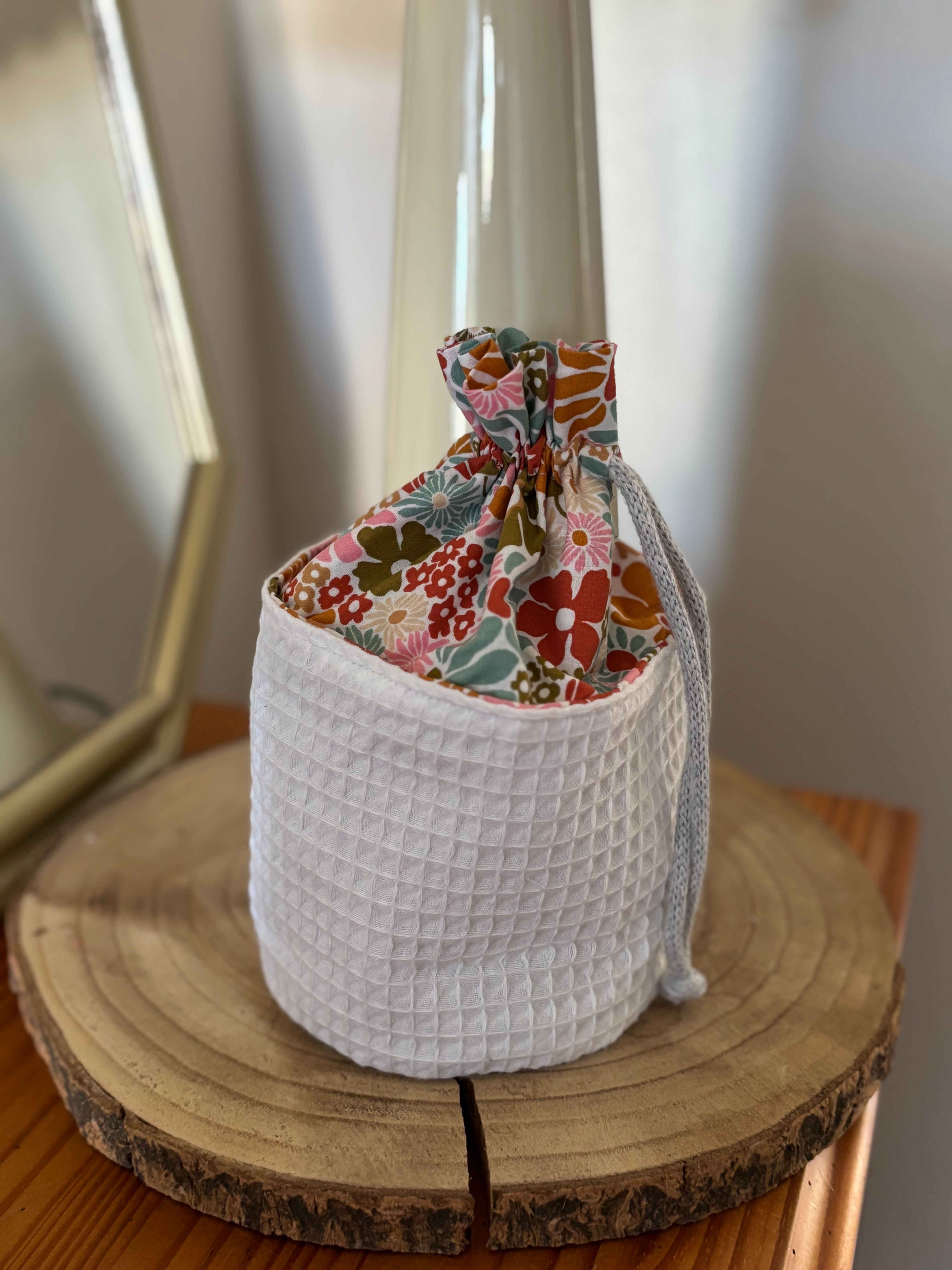 Panier blanc avec tissu fleuri, contenant un objet, sur une surface en bois.