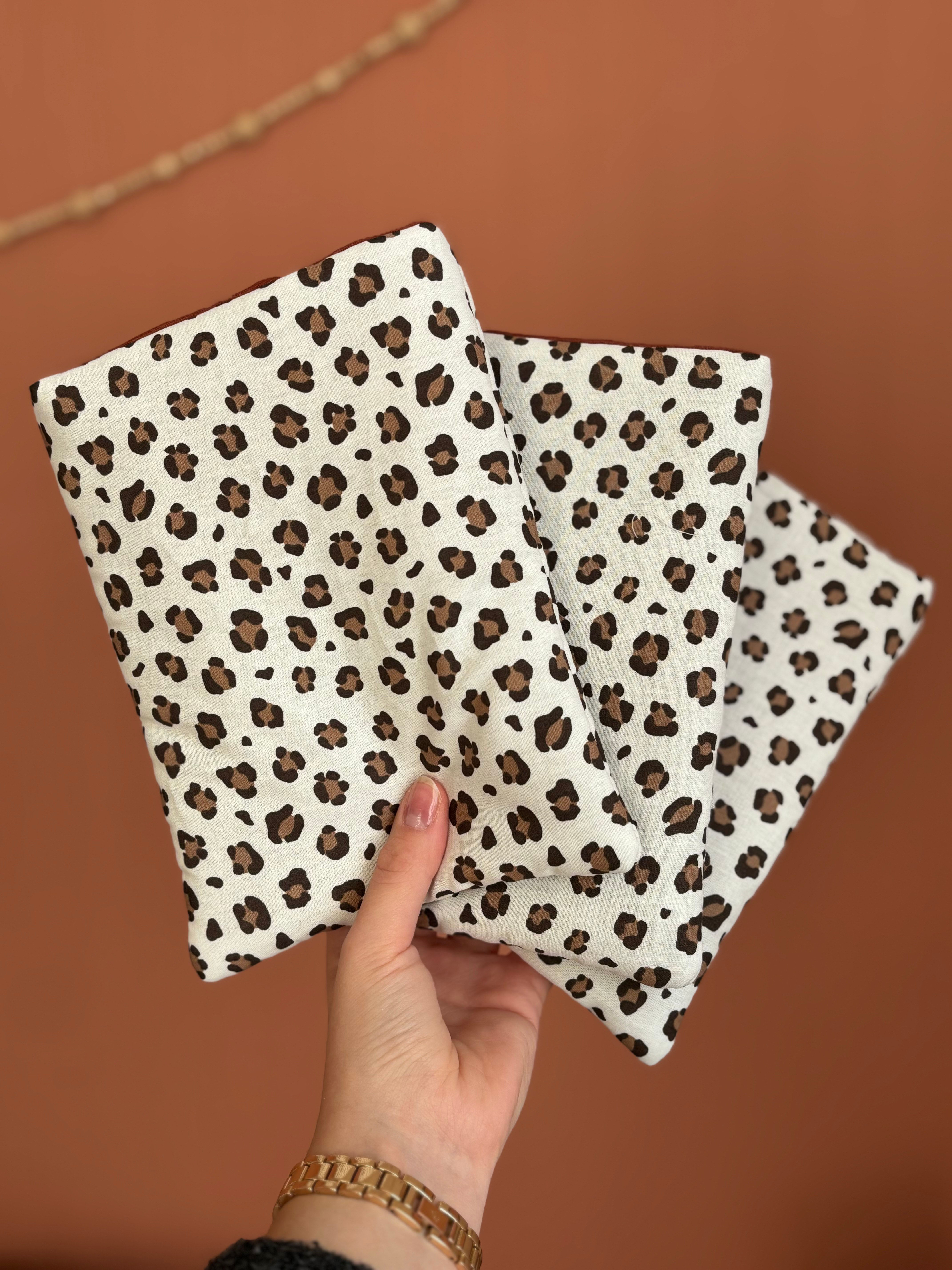 Main tenant trois calot chirurgicals avec motif léopard sur fond marron.