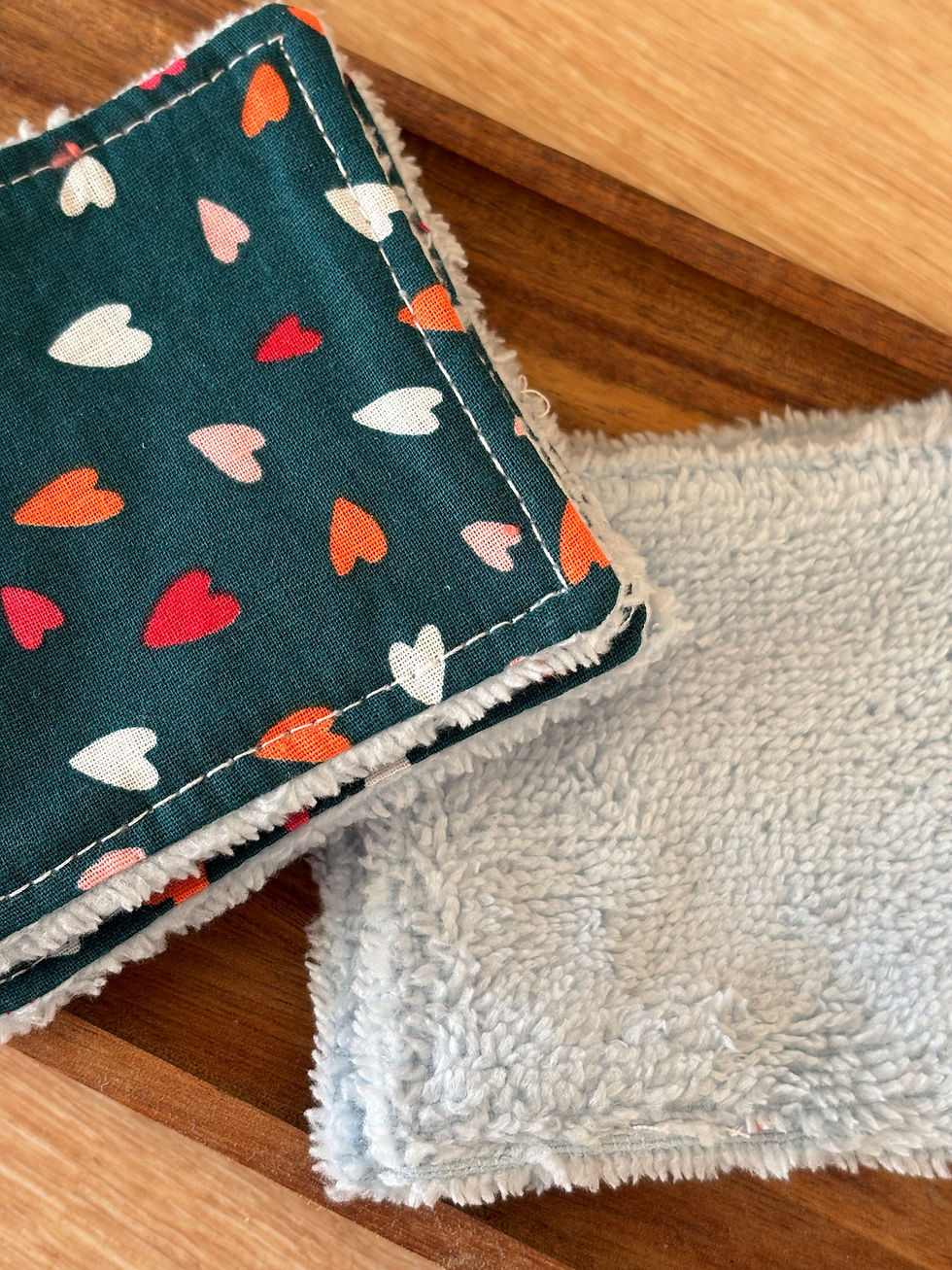 Deux carrés de tissu avec des cœurs colorés et un fond en bois.