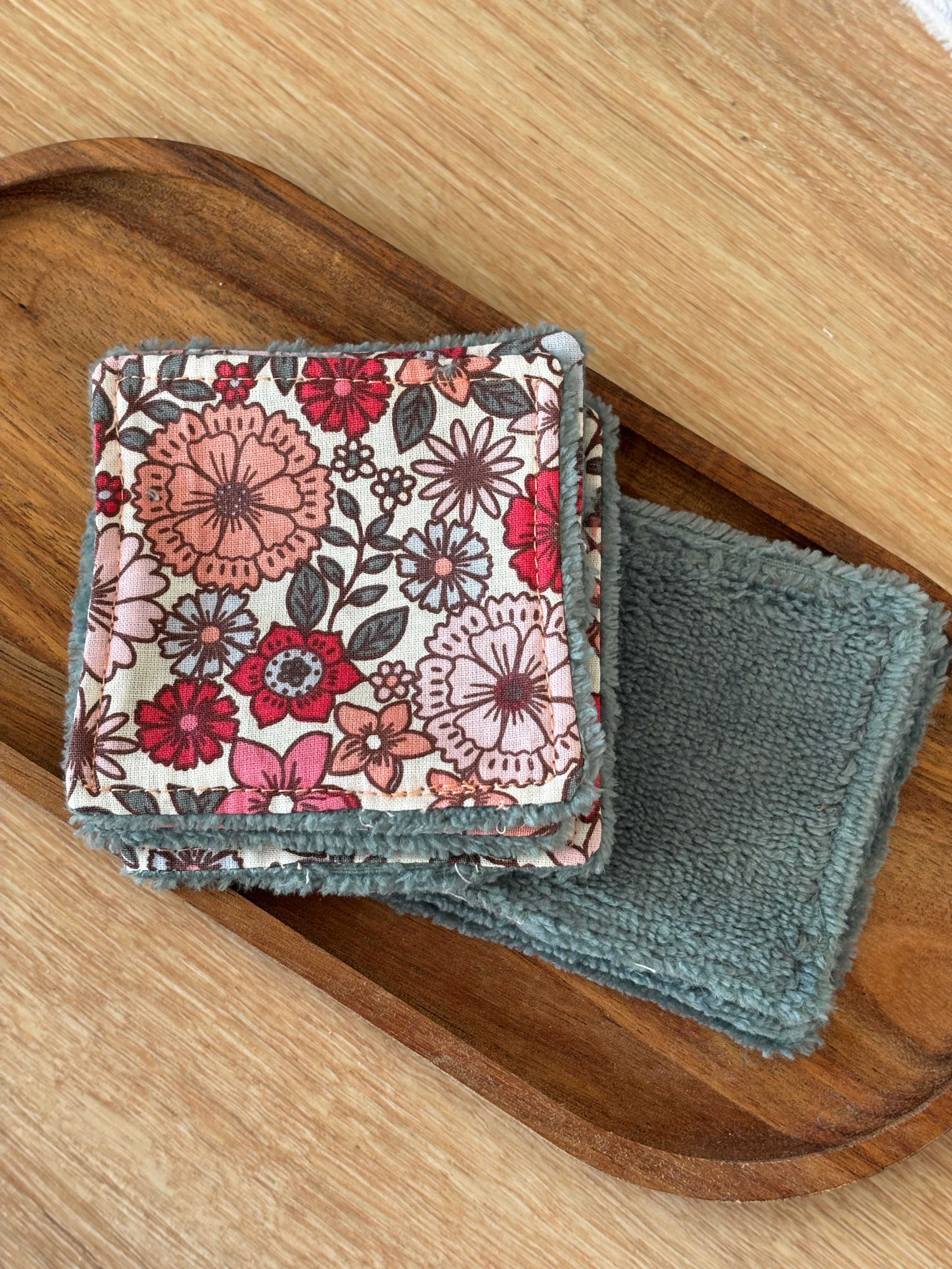 Carrés démaquillants réutilisables avec motif floral rose et gris sur un plateau en bois.