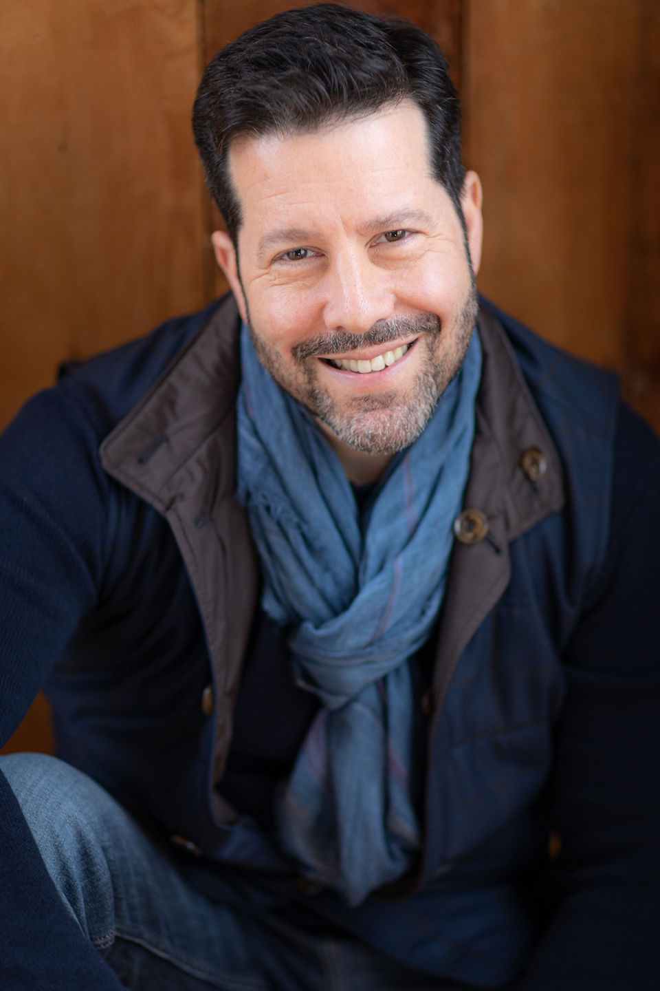 Example of a personable professional photo, man sitting against wooden door in natural light