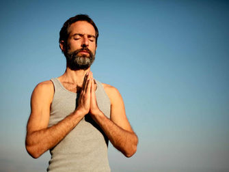 A man stands with his eyes closed and his hands together in a prayer position.