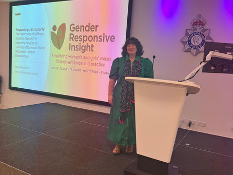 A photo of Lyndsey standing in front of a lectern at the first event she spoke at following Gender Responsive Insight launch. There is a powerpoint slide displayed behind with the consultancy logo
