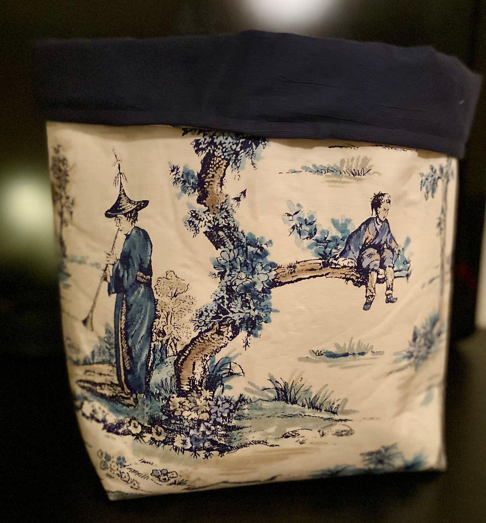 Fabric basket with a charming pastoral scene, featuring a figure in traditional attire playing an instrument and a child sitting on a tree branch, set against a soft cream background.