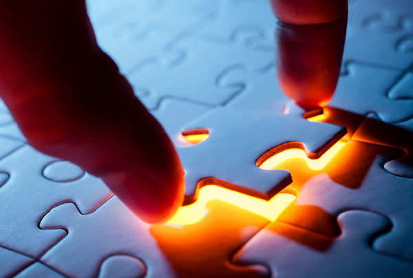 zwei Finger setzten ein Puzzelteil in ein blaues Puzzel ein
