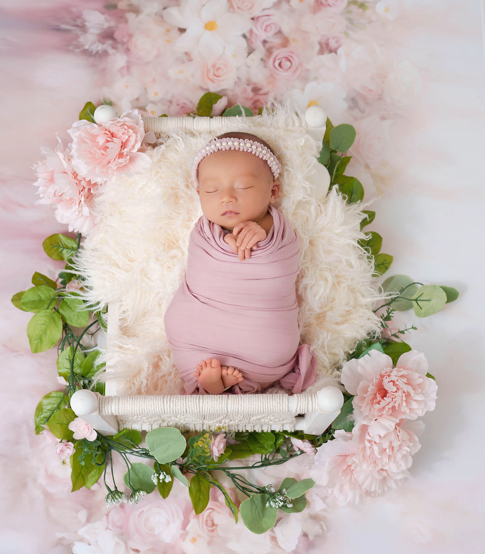 Newborn baby girl pink wrap on white macrame bed surrounded by pink roses and florals — newborn photographer McLean VA