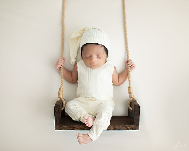 Newborn baby boy, serene and peaceful swinging on a wooden swing.