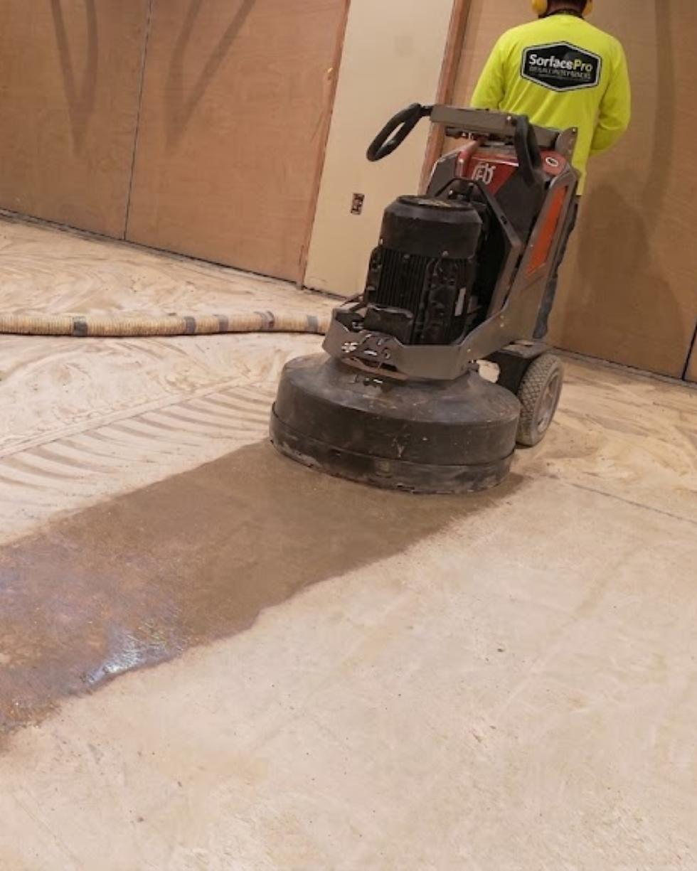 An industrial planetary diamond grinding machine profiling a raw concrete garage floor to open its pores and repair surface cracks, creating a light dust cloud during surface preparation.