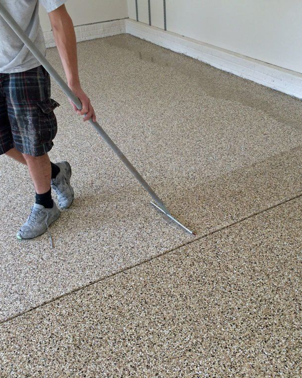 A close-up side-by-side shot of a clear, high-gloss polyaspartic top coat being rolled over a fully flaked garage floor to provide a durable, anti-slip safety texture.