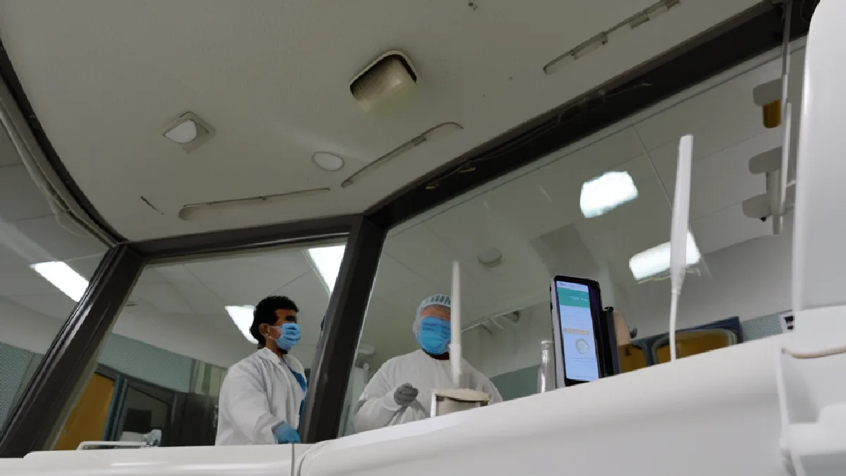 Anonymous researcher checks monitoring equipment in a clinical room prepared for tightly supervised trial safety procedures.