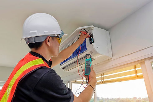 A man wearing a hard hat is working on an air conditioner indoors.