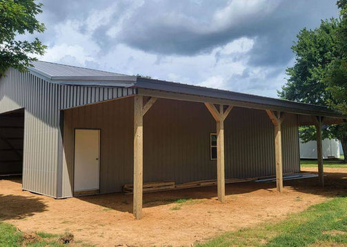 Gray barn structure with door and awning; JC Pole Barns in a field.