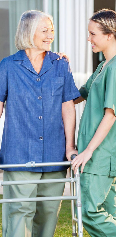 Female caregiver supporting an older woman with a walker during home care mobility assistance.