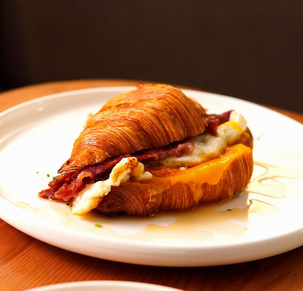 A croissant on a plate that has the filling of beef bacon, egg and cheese