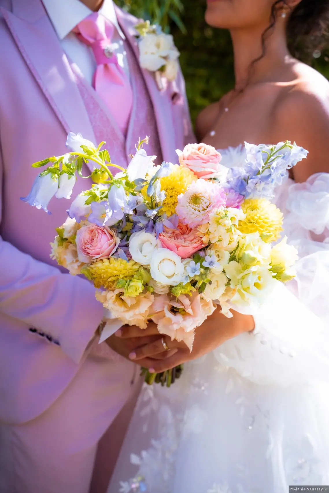 zoom sur le bouquet de marié couleur pastel, les mariés tiennent ensemble le bouquet et se regardent dans les yeux 