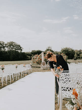 Une wedding planner qui installe le bouquet bout de banc d'une cérémonie laïque en extérieur à un mariage