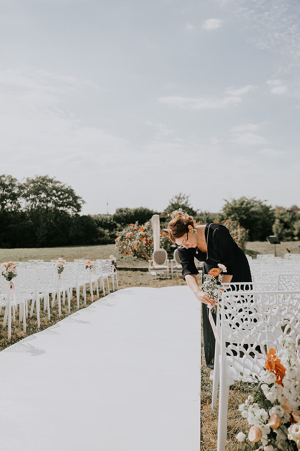 Une wedding planner qui installe le bouquet bout de banc d'une cérémonie laïque en extérieur à un mariage