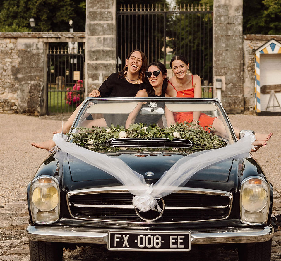 3 wedding planner qui rigolent sur une voiture ancienne