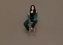 Dark haired woman posing on a wooden stool on a brown background