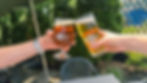 Two people clinking their beers together in a cheers on the patio