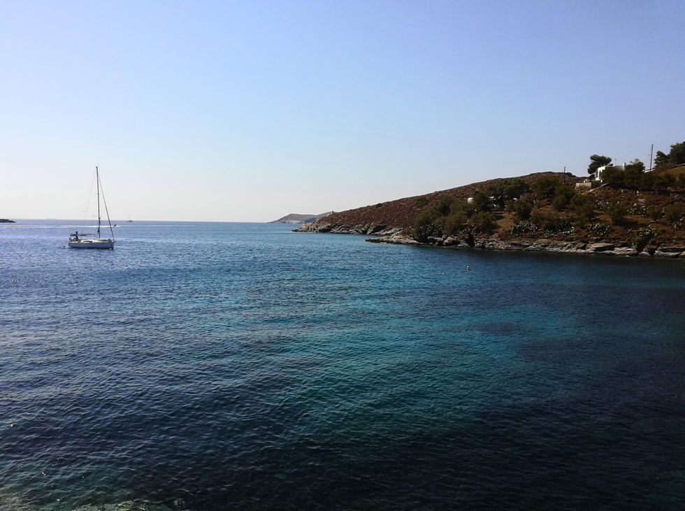 A serene coastal scene shows a clear blue sea with a sailboat.
