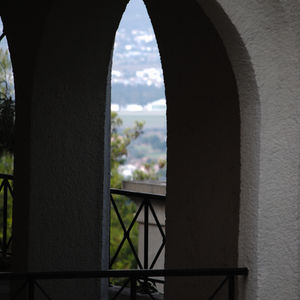 A stone archway frames a serene view of distant hills and trees. The foreground features a metal railing, blending architectural elegance with natural beauty.