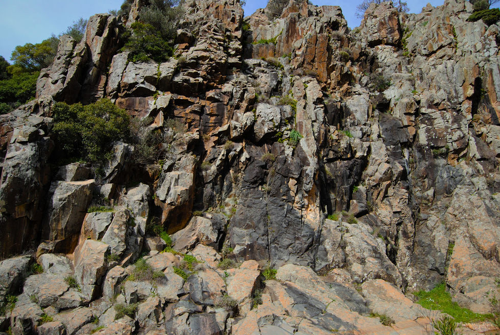 Rocky cliff face with jagged, multicolored stones, interspersed with patches of green vegetation. The scene conveys rugged and natural beauty.