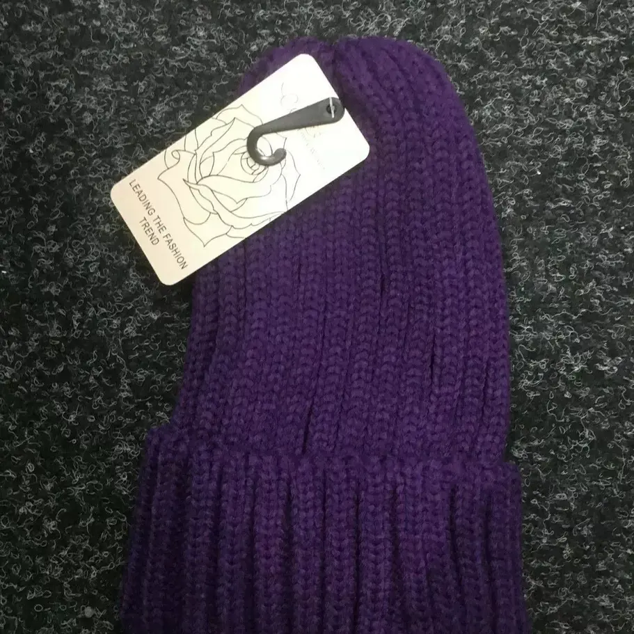 A close-up of the women’s knitted beanie showing the details of the knit pattern, the faux fur pom-pom attachment, and the i