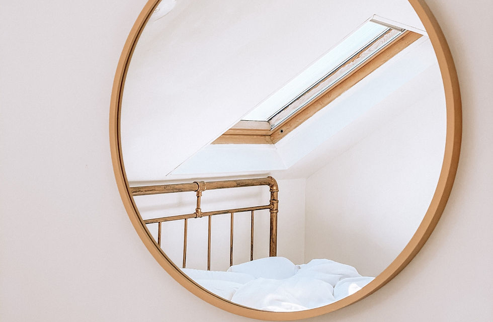 Round gold mirror reflecting a metal bed frame and skylight