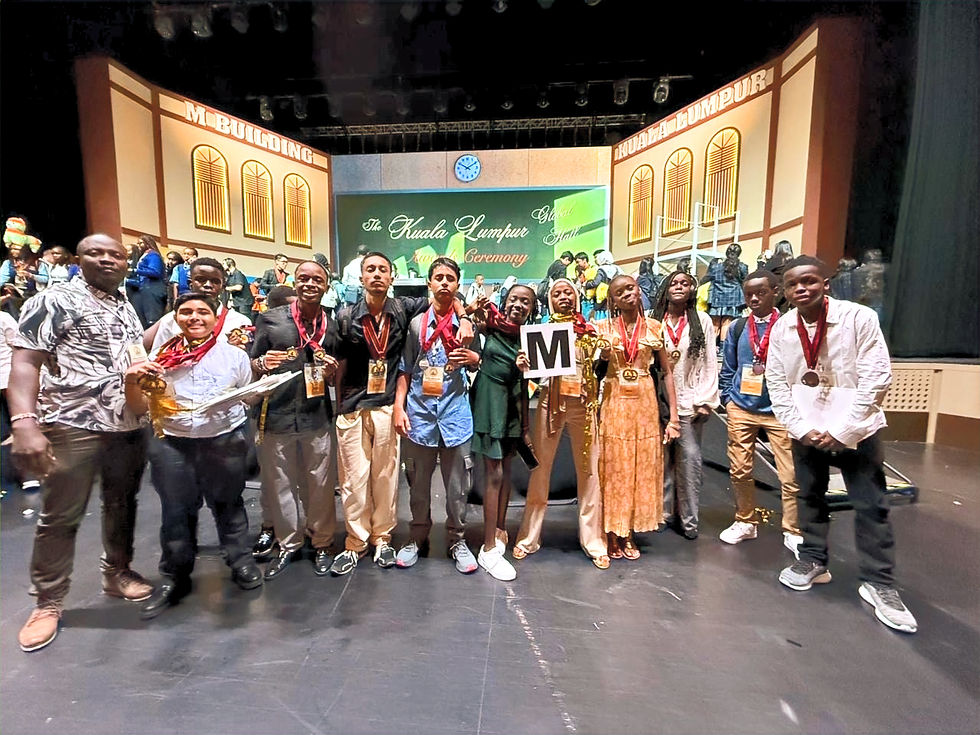 Jalaram Academy students proudly pose at an event in Kuala Lumpur, showcasing their achievements with medals around their necks and excited smiles on stage.