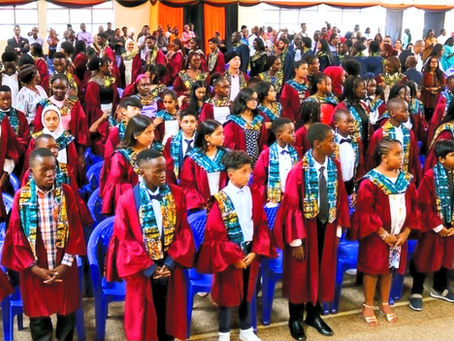 Graduates in vibrant gowns stand proudly in a bustling hall, ready to celebrate their achievements amidst a supportive gathering of family and friends.