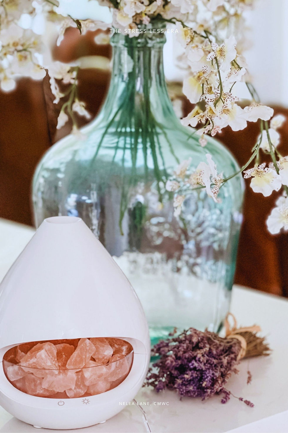 Nelea Lane's PureGlow Himalayan salt and essential oil diffuser on a white surface styled with a green glass vase and dried lavender — part of The Stress Less Era calm home ritual.