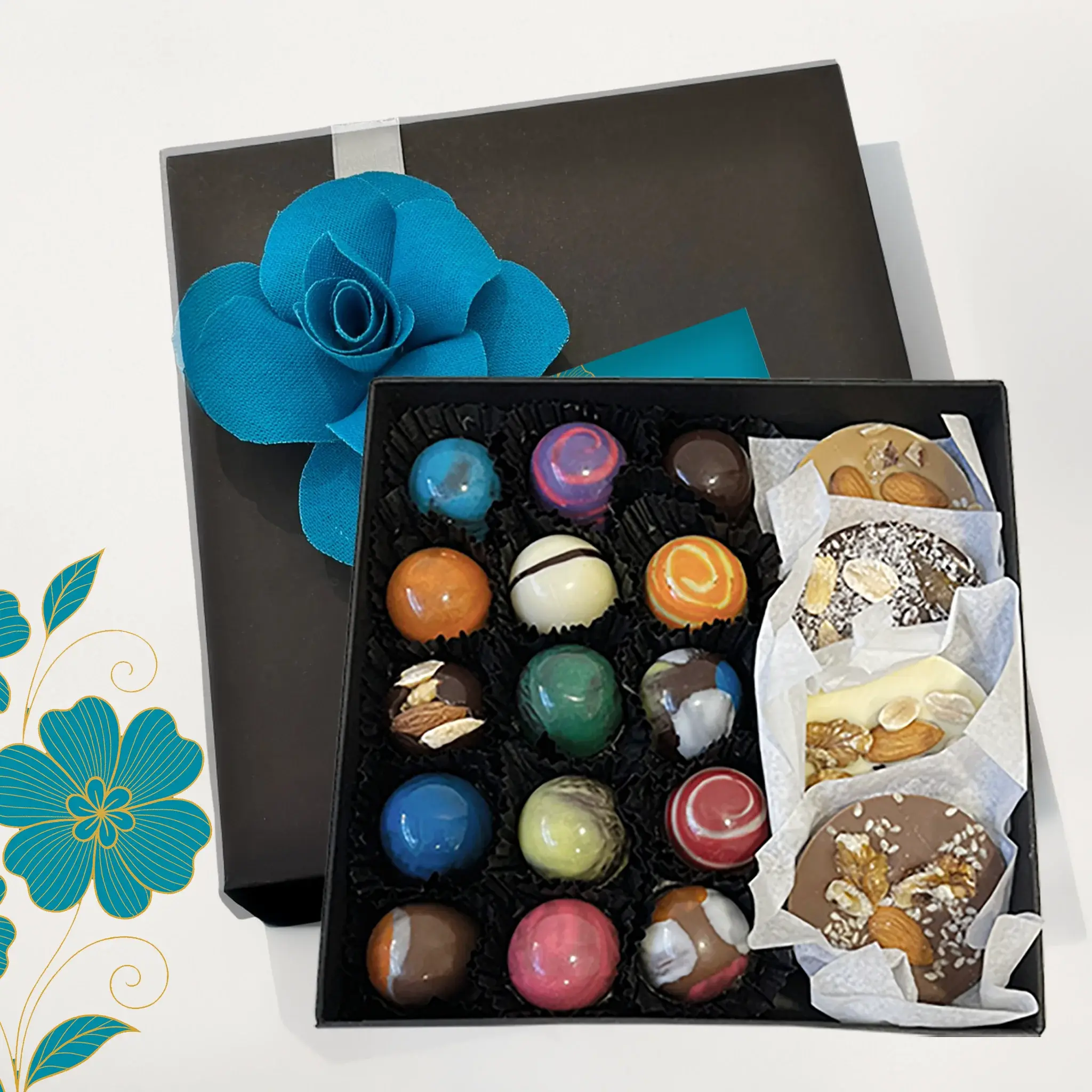 Caja negra abierta con bombones artesanales de colores, decorada con una flor de tela azul.