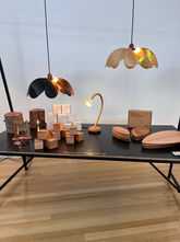 Small hand sized objects are displayed on a black table, and include wooden boxes, flat wooded board shaped like flower petals, and various lights.
