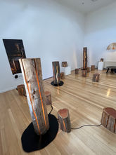 A series of tree trunks and stumps are spread across a wooden floored room. Cracks running up the trunks and stumps allow light to shine out.