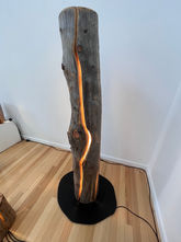 A close up of a tall and slender Trunk light standing by a white wall. A curving crack allows light to shine out from within.